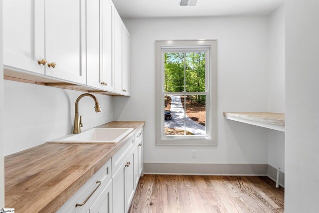 laundry room with baseboards, visible vents, a sink, and light wood finished floors
