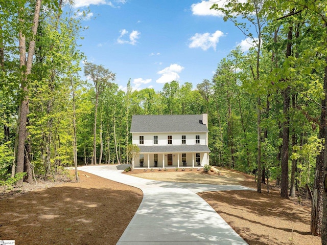 view of front of home featuring a forest view, a shingled roof, and covered porch