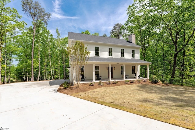 view of front of house with driveway, a chimney, and covered porch