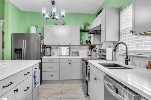 kitchen with under cabinet range hood, stainless steel appliances, light countertops, a sink, and tasteful backsplash