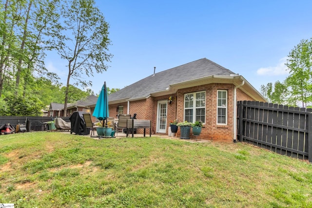 back of house with a shingled roof, a fenced backyard, a patio, a lawn, and brick siding