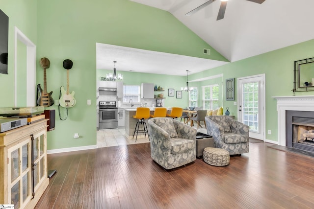 living area featuring light wood-style flooring, visible vents, high vaulted ceiling, ceiling fan with notable chandelier, and a fireplace