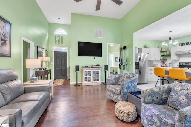 living area featuring wood finished floors, a towering ceiling, visible vents, and ceiling fan with notable chandelier