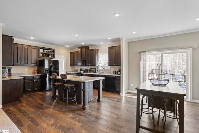 kitchen featuring a center island, crown molding, black appliances, dark brown cabinetry, and a kitchen bar
