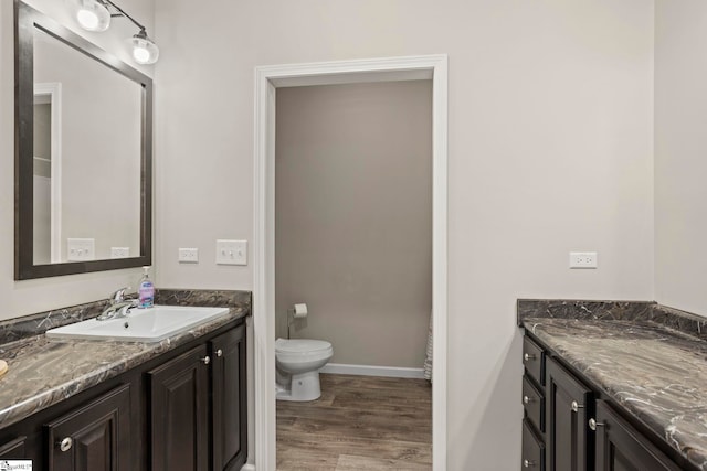 bathroom featuring baseboards, wood finished floors, vanity, and toilet