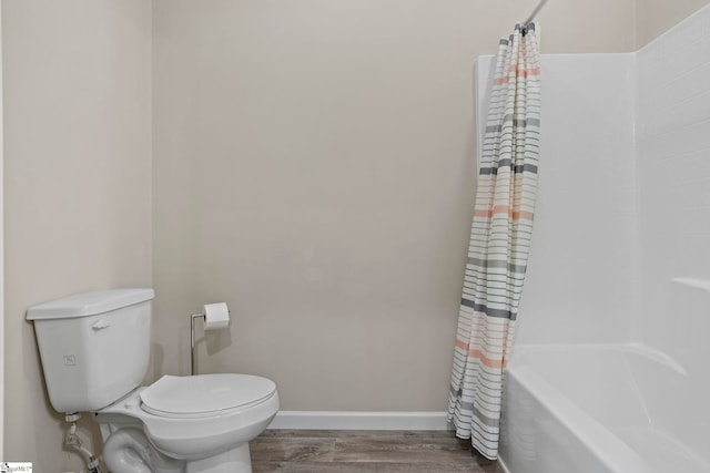 bathroom with shower / tub combo, toilet, wood finished floors, and baseboards