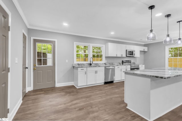 kitchen with white cabinets, light stone counters, ornamental molding, a sink, and appliances with stainless steel finishes