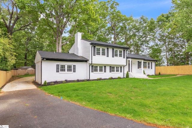 tri-level home with a chimney, fence, aphalt driveway, and a front yard