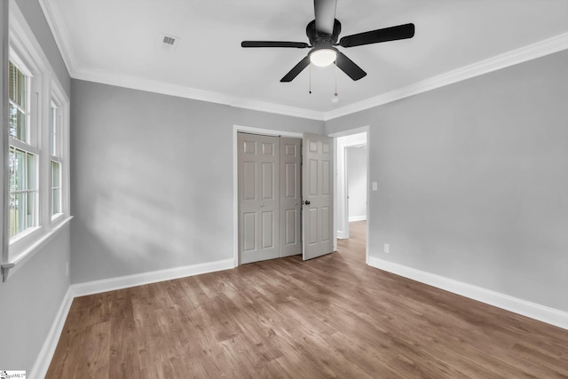 unfurnished bedroom featuring baseboards, ornamental molding, wood finished floors, and a closet