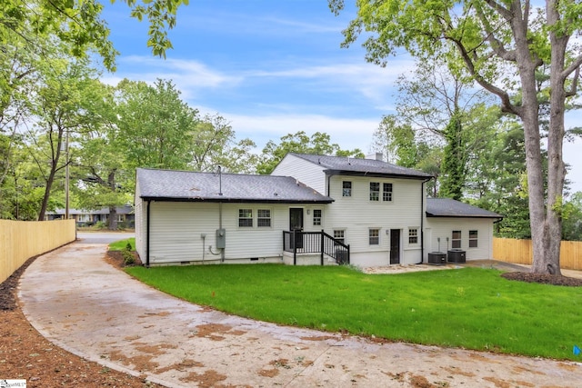 rear view of house with a lawn, concrete driveway, a chimney, and fence