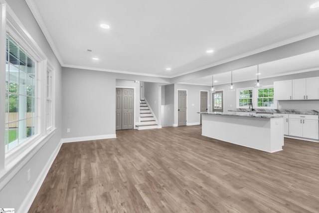 unfurnished living room featuring baseboards, ornamental molding, wood finished floors, and stairs