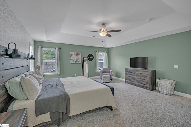 carpeted bedroom featuring baseboards, a tray ceiling, ceiling fan, and multiple windows