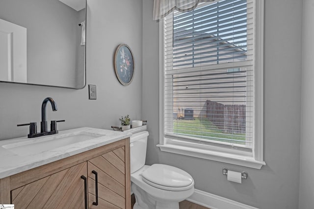 half bath with baseboards, a healthy amount of sunlight, vanity, and toilet