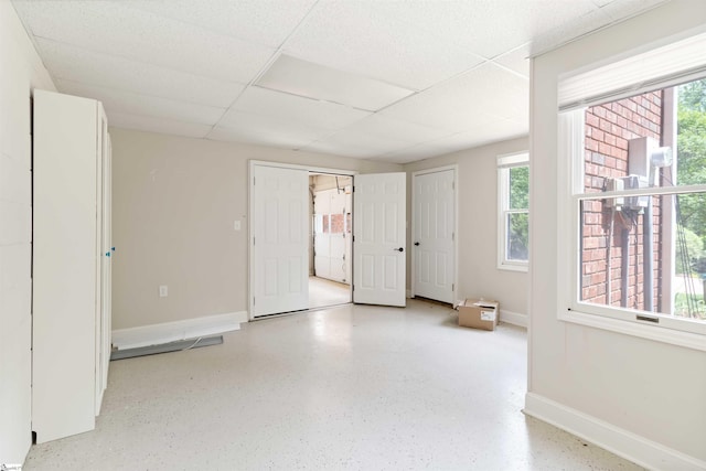 empty room with speckled floor, a drop ceiling, and baseboards