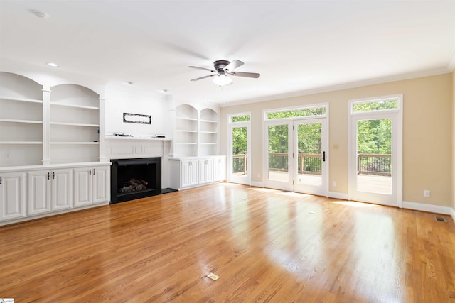 unfurnished living room with crown molding, light wood-type flooring, ceiling fan, a fireplace, and baseboards