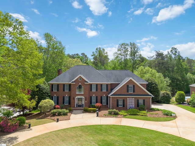 view of front of home featuring a front lawn, a chimney, curved driveway, and brick siding