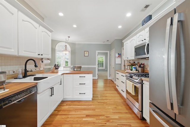 kitchen with stainless steel appliances, a peninsula, a sink, light wood-type flooring, and recessed lighting