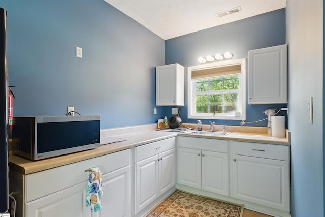 kitchen featuring a sink, stainless steel microwave, visible vents, white cabinetry, and light countertops