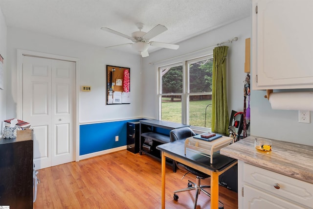 home office with light wood-type flooring, a textured ceiling, baseboards, and ceiling fan