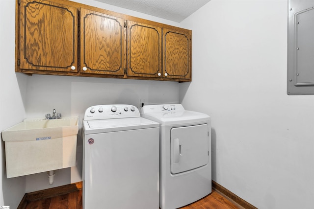 laundry area with wood finished floors, a sink, electric panel, washer and dryer, and cabinet space