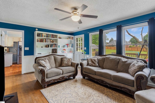 living room featuring light wood-style floors, a textured ceiling, a ceiling fan, and a wainscoted wall
