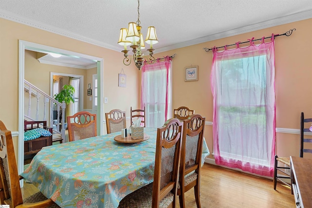 dining area featuring stairway, a textured ceiling, light wood-style floors, an inviting chandelier, and ornamental molding