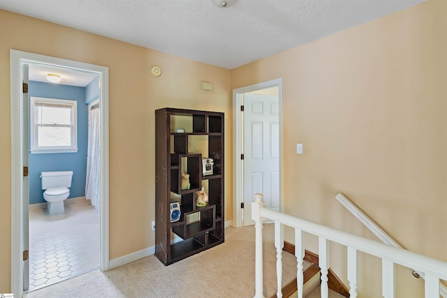 hall with carpet floors, an upstairs landing, a textured ceiling, and baseboards