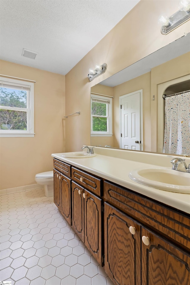 bathroom featuring toilet, a sink, visible vents, and double vanity