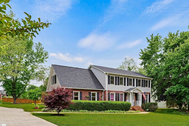 colonial home with fence, a front lawn, brick siding, and roof with shingles
