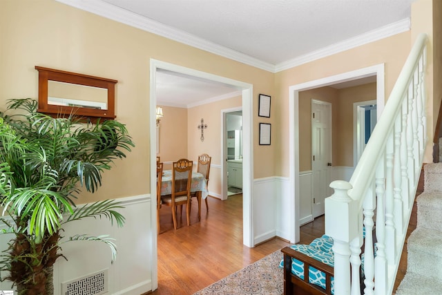 corridor with crown molding, stairs, wood finished floors, a wainscoted wall, and visible vents