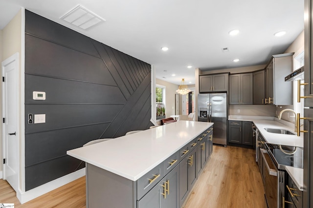 kitchen with a kitchen island, stainless steel appliances, light wood finished floors, and a sink