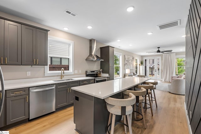 kitchen featuring stainless steel appliances, wall chimney range hood, visible vents, a sink, and open floor plan