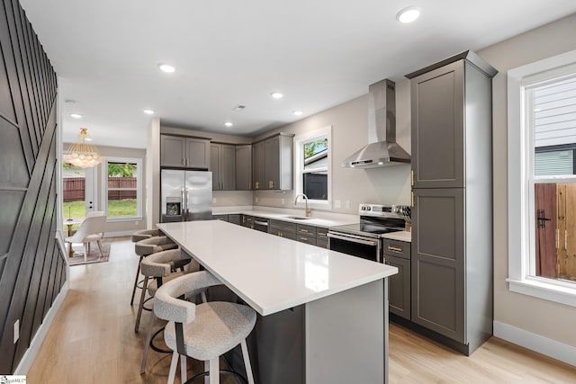 kitchen with stainless steel appliances, light wood-style flooring, a kitchen breakfast bar, a sink, and wall chimney range hood