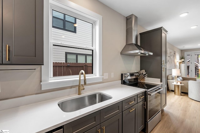 kitchen with light countertops, a sink, wall chimney exhaust hood, stainless steel electric range, and light wood-style flooring