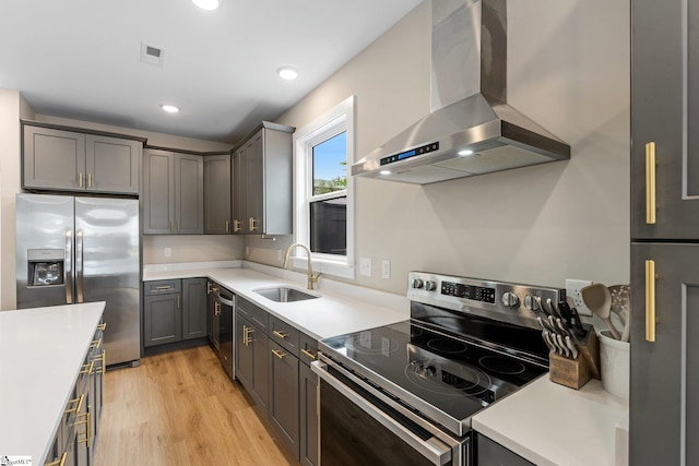 kitchen featuring wall chimney range hood, a sink, light countertops, stainless steel appliances, and light wood-style flooring