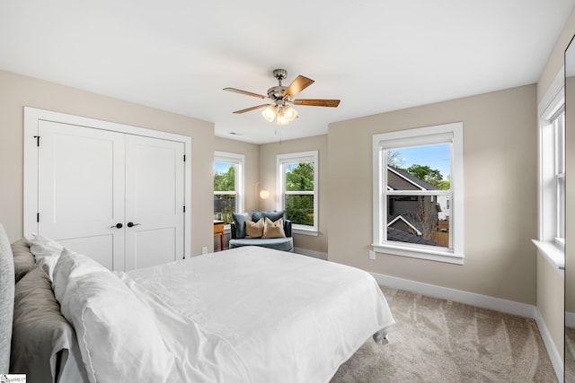 bedroom featuring light colored carpet, ceiling fan, baseboards, and a closet