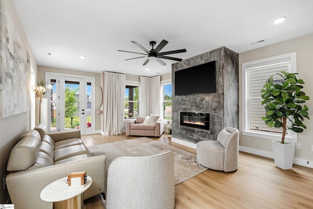 living area featuring a premium fireplace, a ceiling fan, light wood-style flooring, baseboards, and visible vents