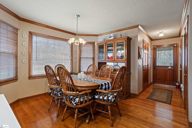 dining space featuring light wood-type flooring, a textured ceiling, ornamental molding, and a notable chandelier