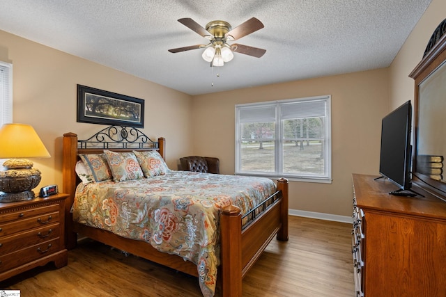 bedroom featuring wood finished floors, a textured ceiling, baseboards, and ceiling fan