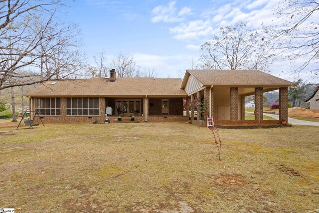 rear view of property with a chimney, a lawn, brick siding, roof with shingles, and a sunroom