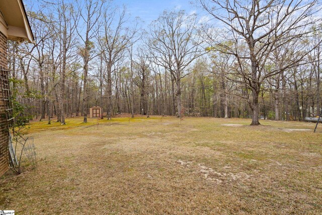 view of yard featuring an outdoor structure, a wooded view, and a storage unit