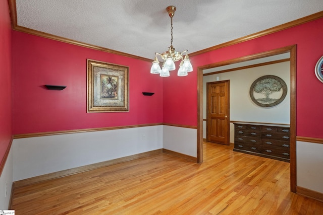 empty room with baseboards, ornamental molding, a chandelier, and light wood-style flooring