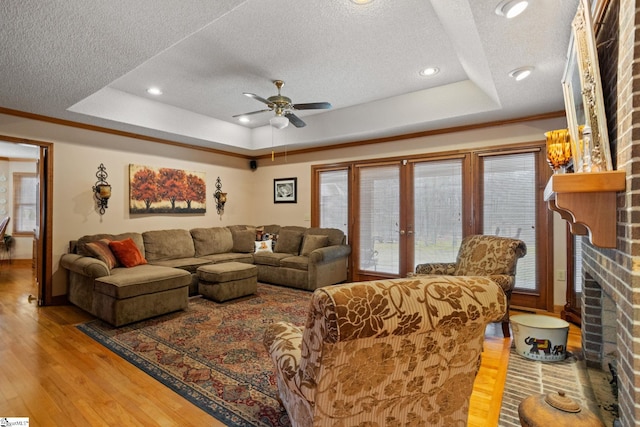 living area featuring a textured ceiling, light wood-type flooring, ceiling fan, a fireplace, and a raised ceiling