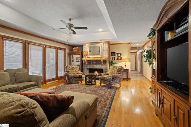 living room with a ceiling fan, a textured ceiling, light wood-type flooring, a tray ceiling, and a fireplace