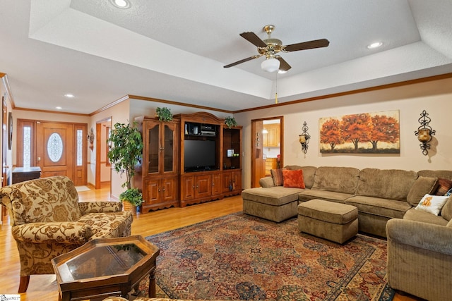 living area with light wood-type flooring, ceiling fan, a raised ceiling, ornamental molding, and recessed lighting