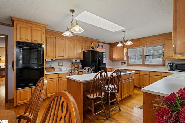kitchen with a skylight, black appliances, light wood-type flooring, light countertops, and a kitchen island
