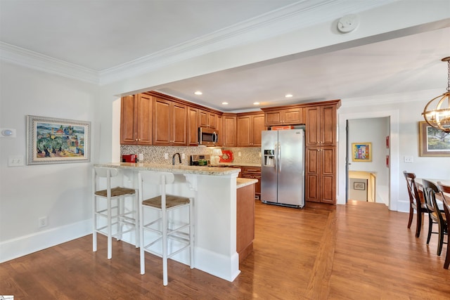 kitchen with brown cabinets, an inviting chandelier, stainless steel appliances, a kitchen bar, and a peninsula