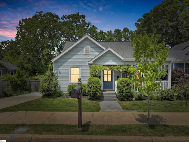 bungalow-style home with fence, a shingled roof, and a front lawn
