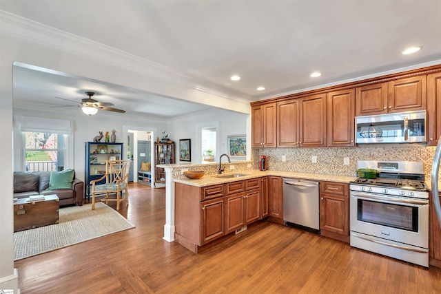 kitchen with stainless steel appliances, ornamental molding, a sink, a peninsula, and open floor plan