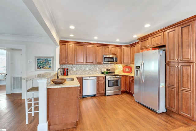 kitchen with stainless steel appliances, a peninsula, a sink, brown cabinets, and ornamental molding